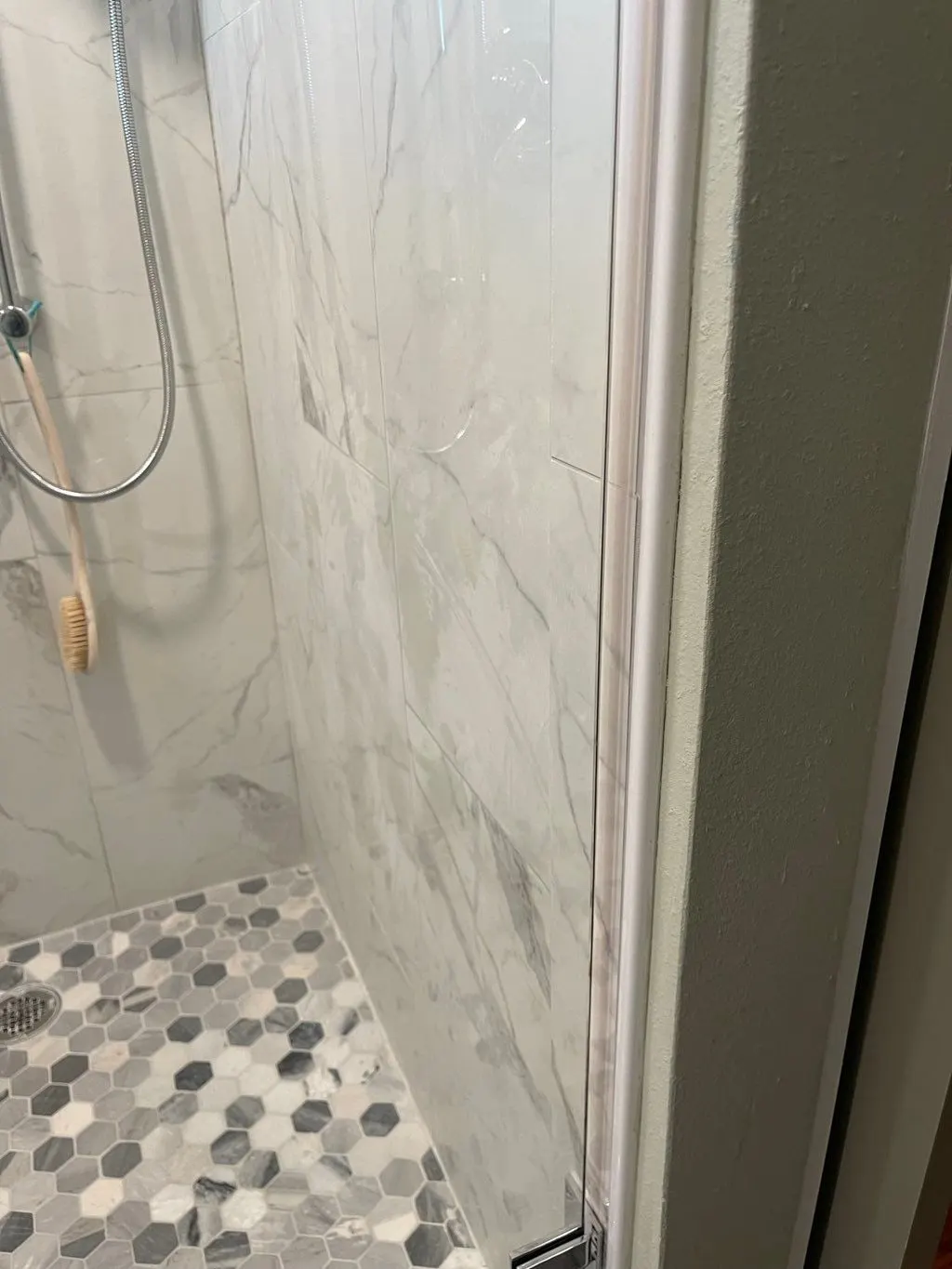 Marble-look shower walls above a gray hexagon mosaic floor
