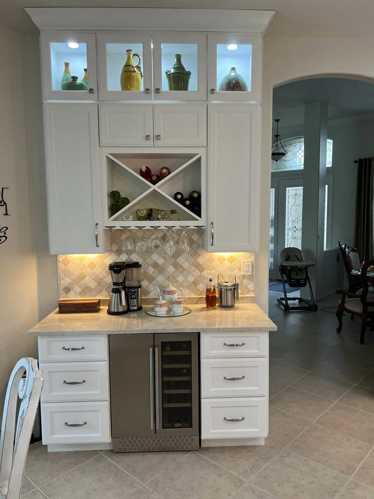 White built-in coffee bar with lit glass-front cabinets, an X wine rack and a wine fridge