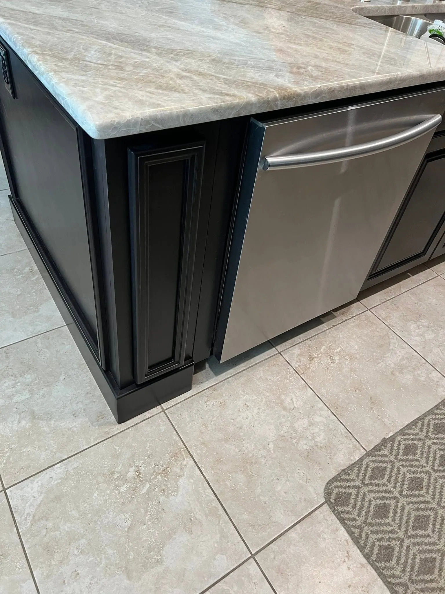 End of a black island with a raised-panel door beside a stainless dishwasher