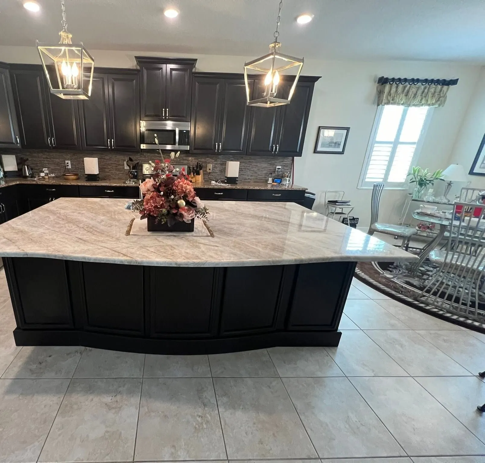 Kitchen with espresso cabinetry, a black paneled island with a light stone top, and two lantern pendants