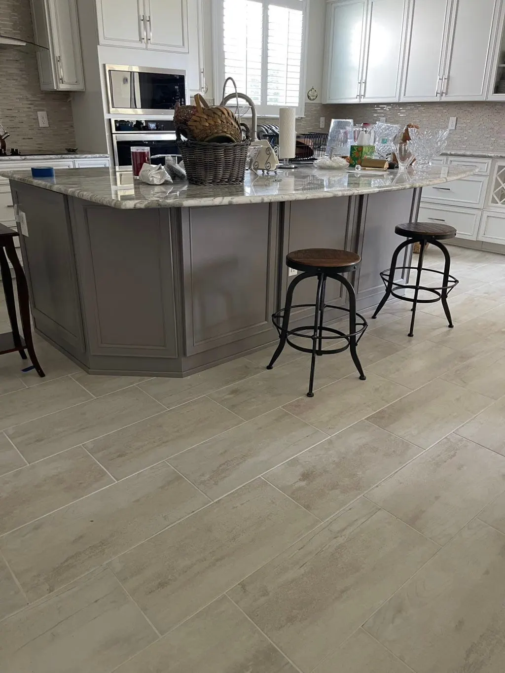 Angled gray island with a granite top and bar stools, white cabinets behind
