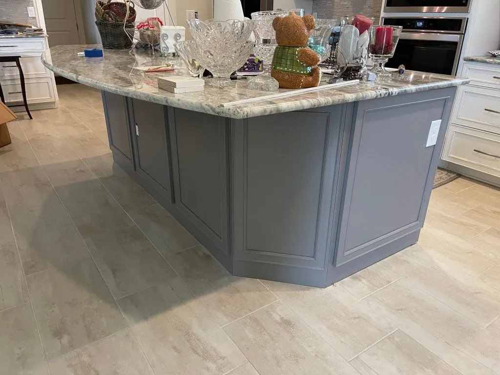Gray painted island with raised panels and a granite top in a white kitchen