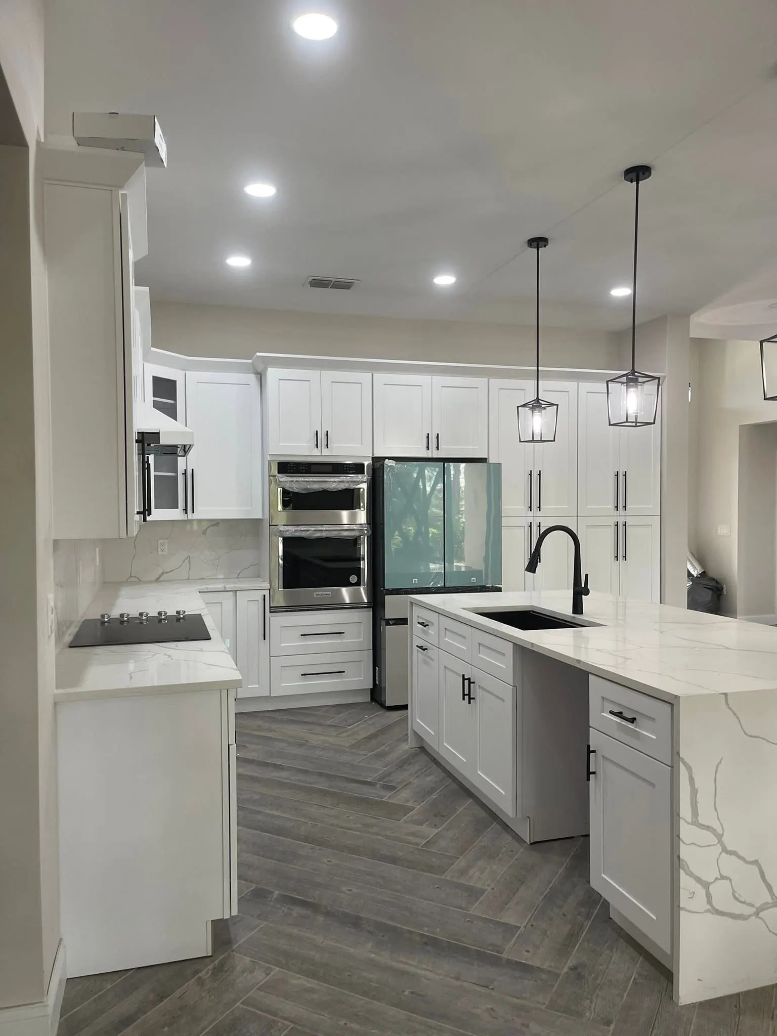 White kitchen with a marble-look waterfall island, pendant lights and tall pantry cabinets