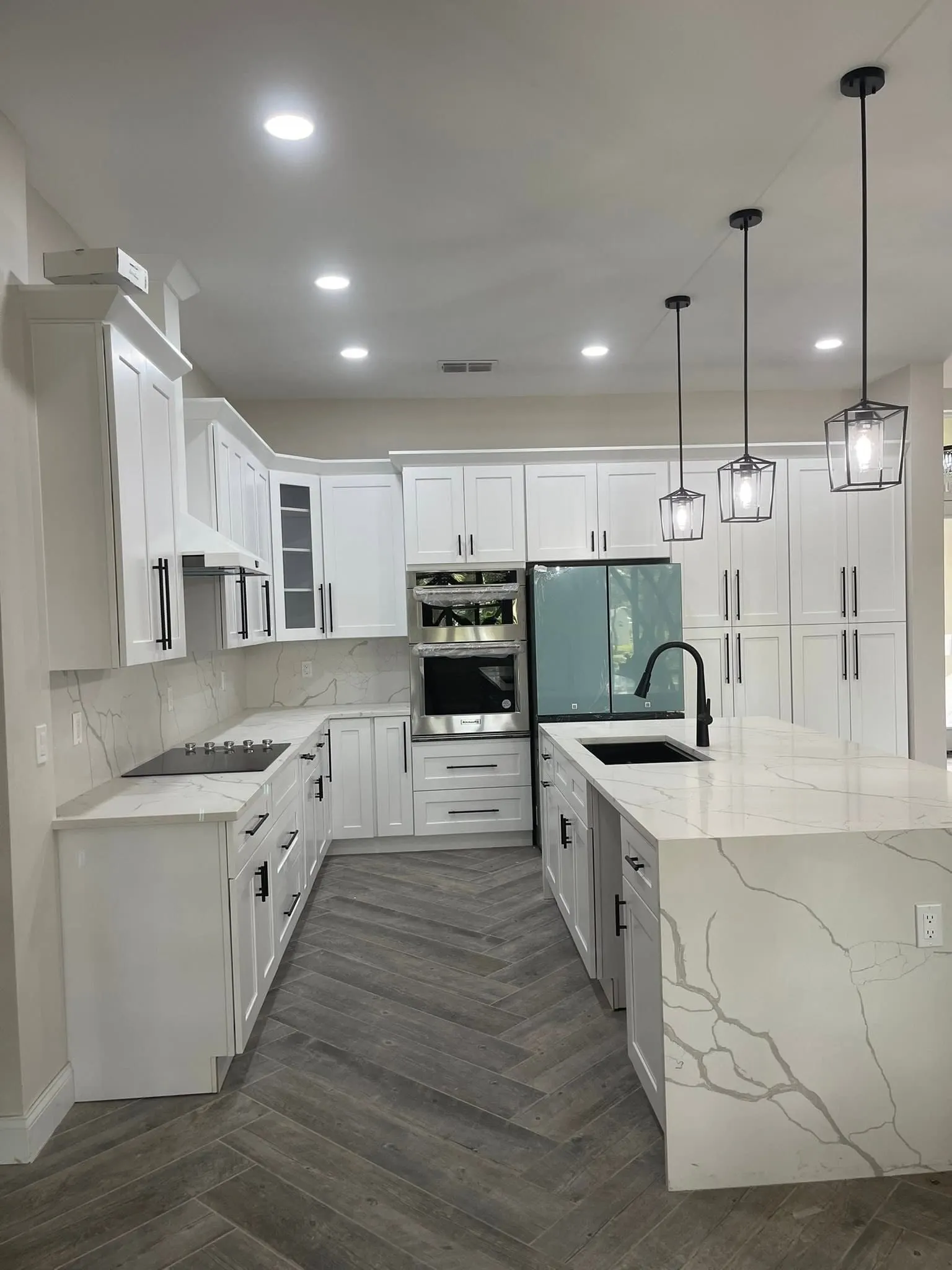 White kitchen with three pendant lights over a marble-look waterfall island