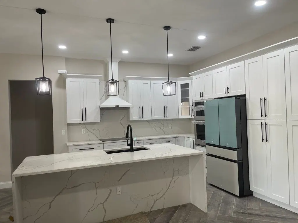 White kitchen with black pendant lights over a marble-look waterfall island