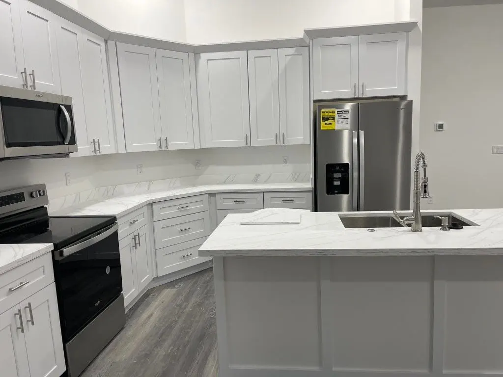 White shaker kitchen with corner cabinets, stainless appliances and an island
