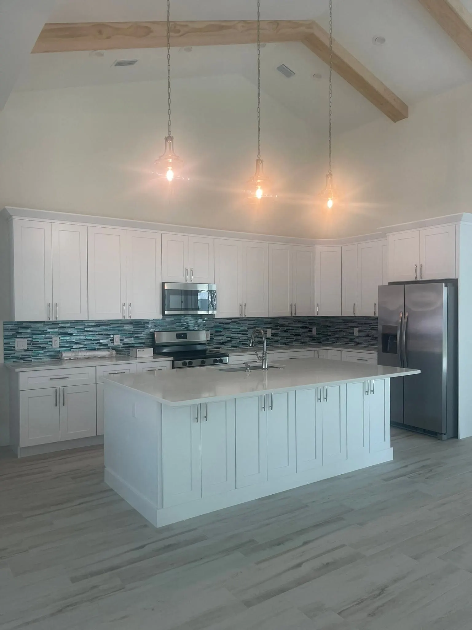 White kitchen island with pendant lights hanging from a wood beam