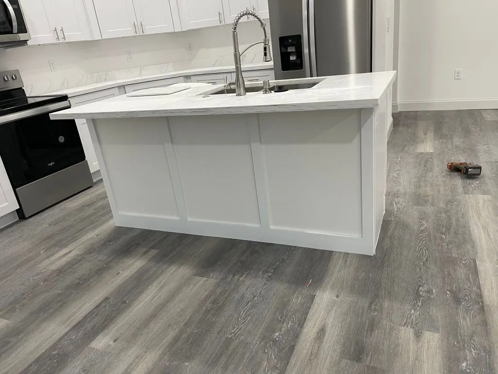 White kitchen island with a white quartz top on gray plank floors