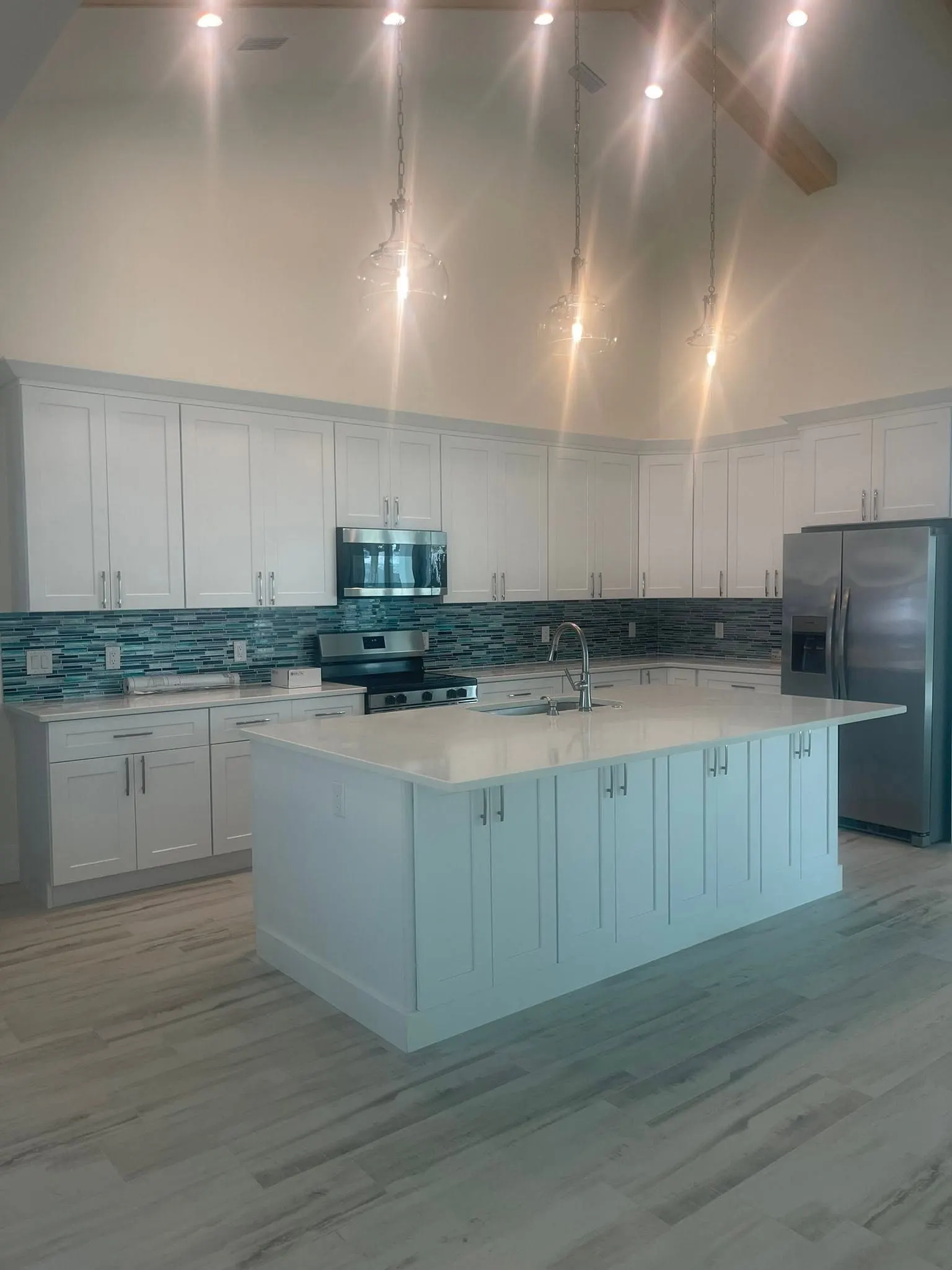 White kitchen with a large island and blue glass tile backsplash under a vaulted ceiling