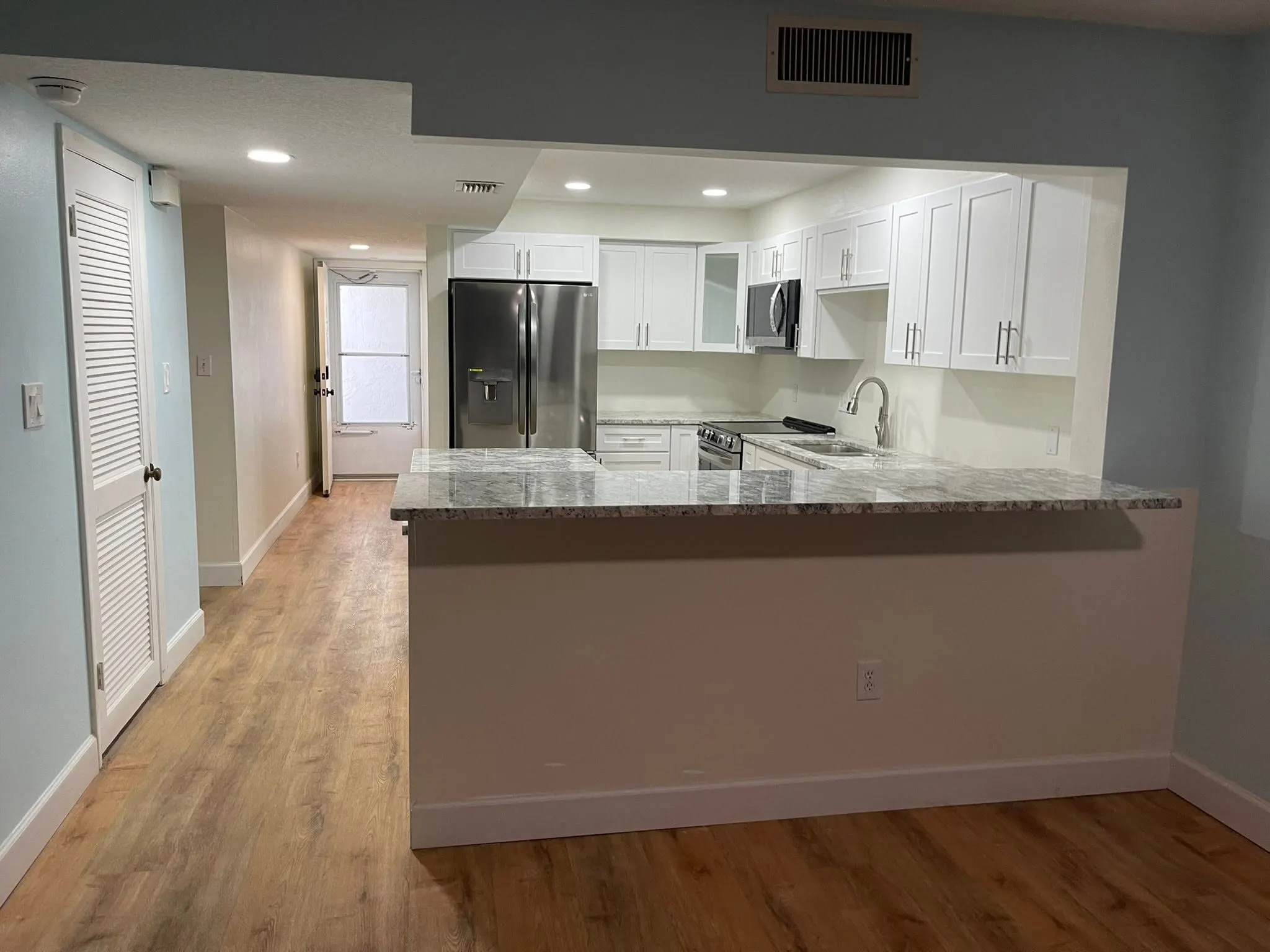 Open white kitchen with a granite peninsula and wood-look floors