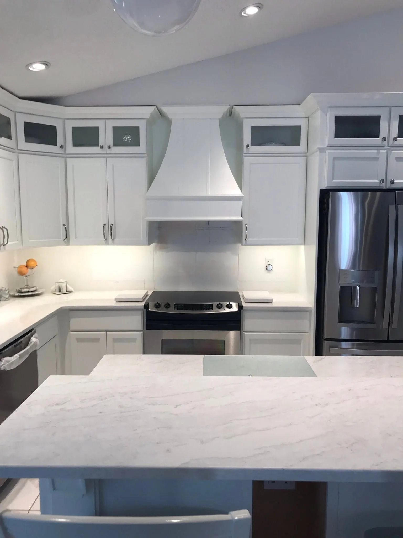 White kitchen with a paneled range hood and glass-front uppers above the island