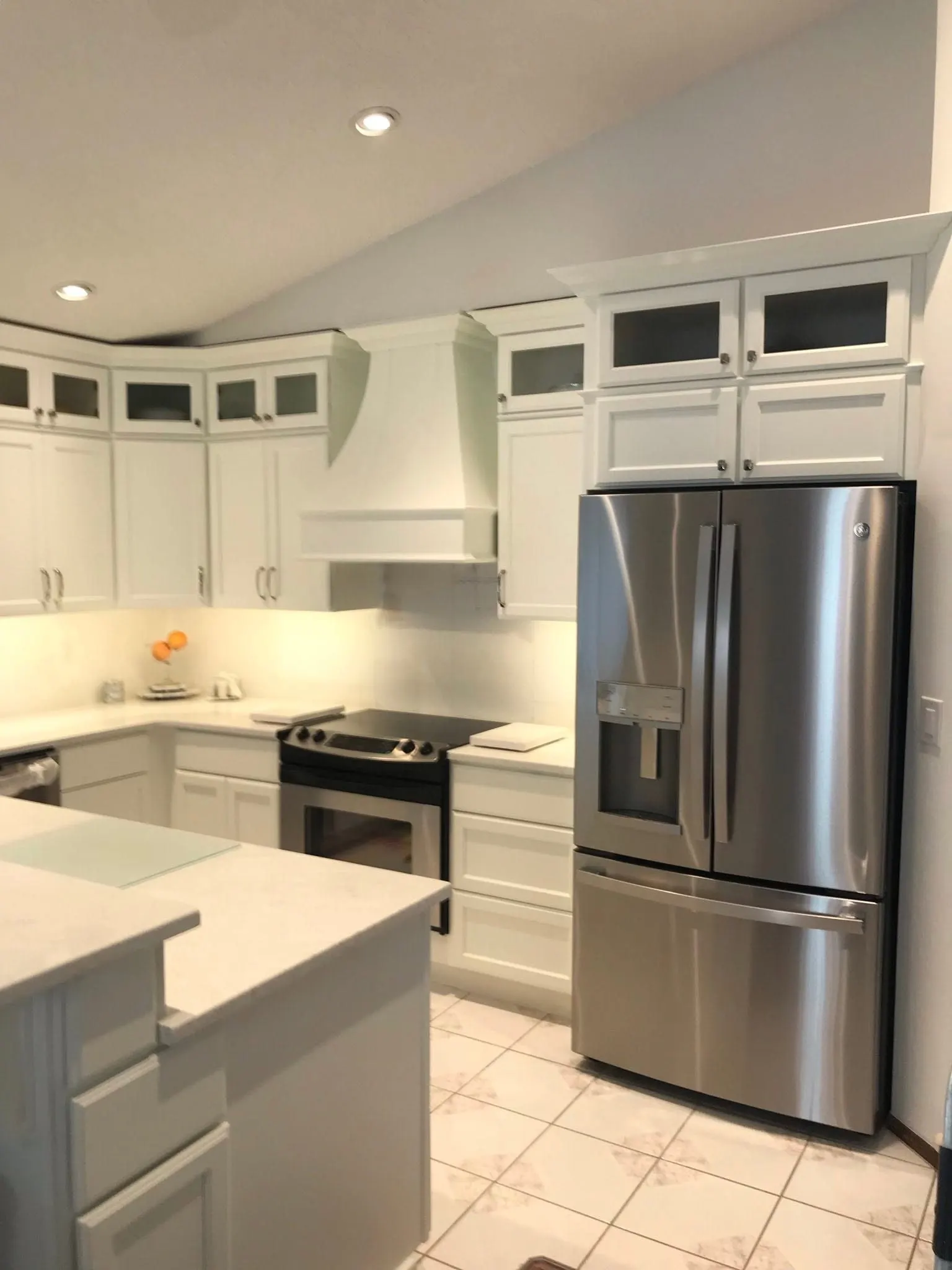 White shaker kitchen under a vaulted ceiling, with glass-front uppers and a stainless refrigerator
