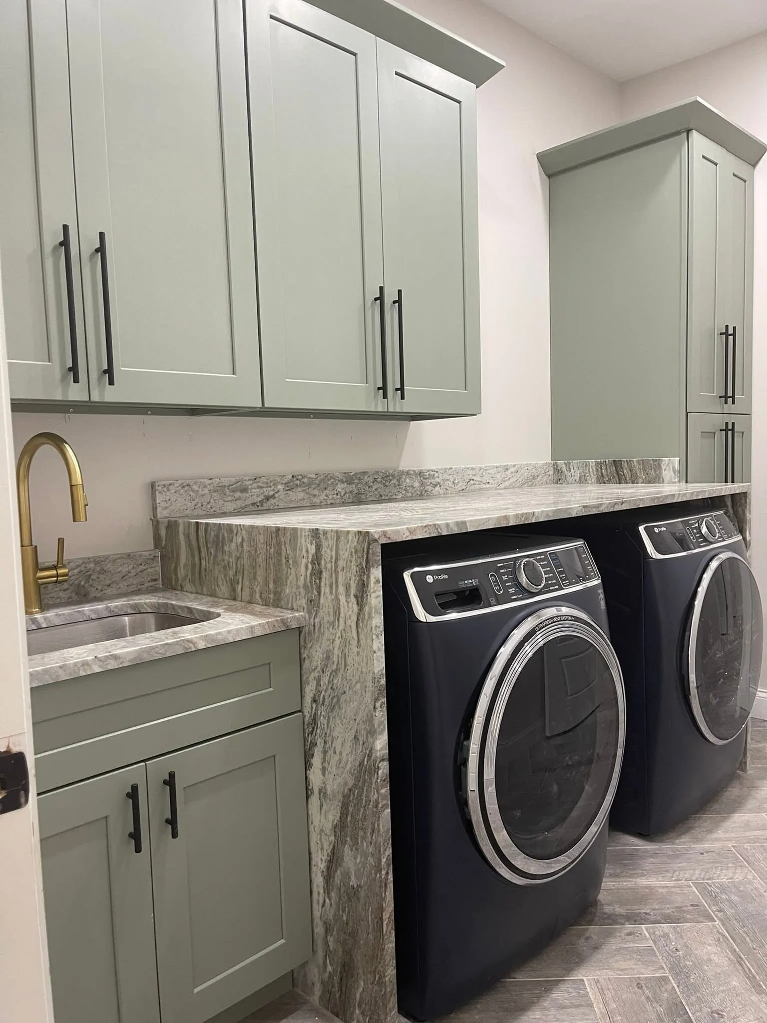 Sage green laundry cabinets with a stone waterfall counter over the washer and dryer