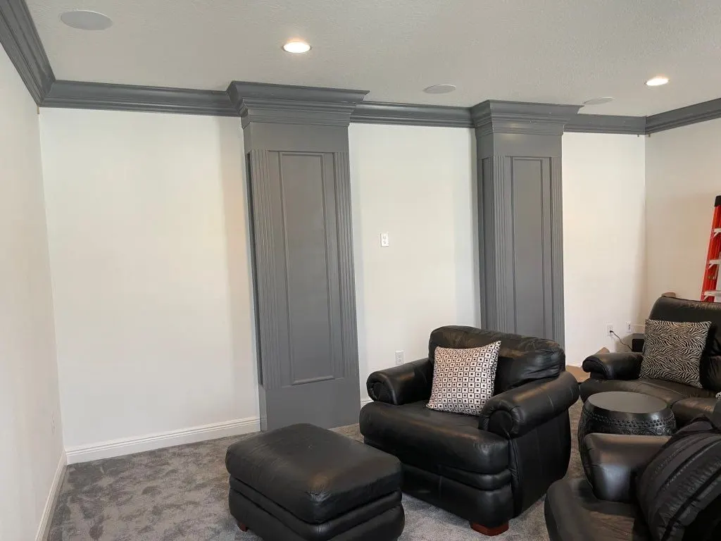Media room with gray paneled columns, crown molding and leather recliners