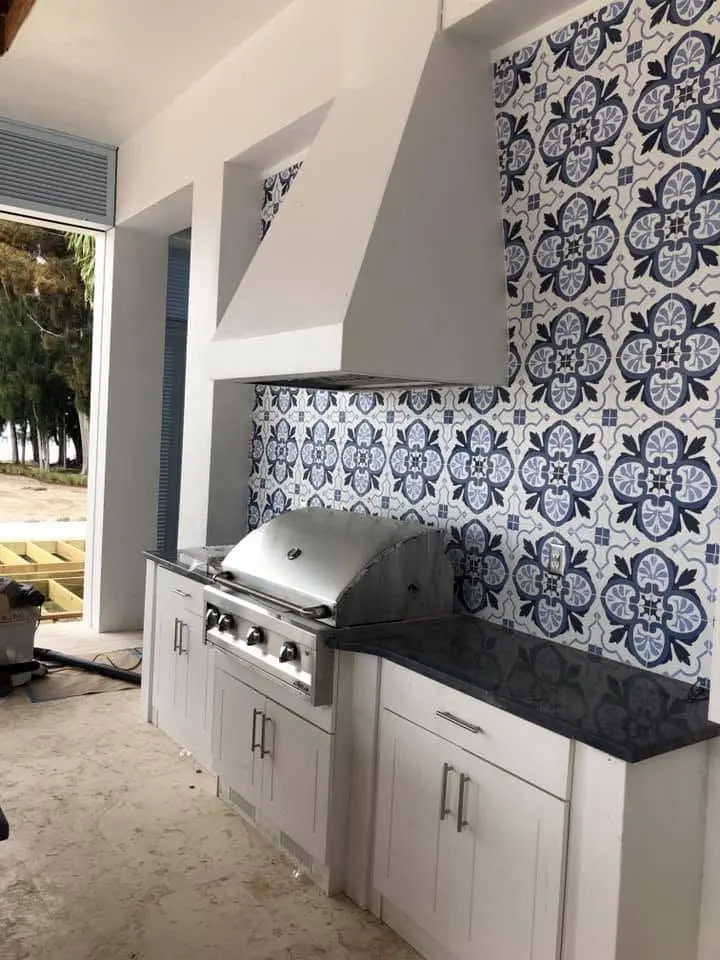 Built-in stainless grill in white outdoor cabinetry under a blue tile backsplash