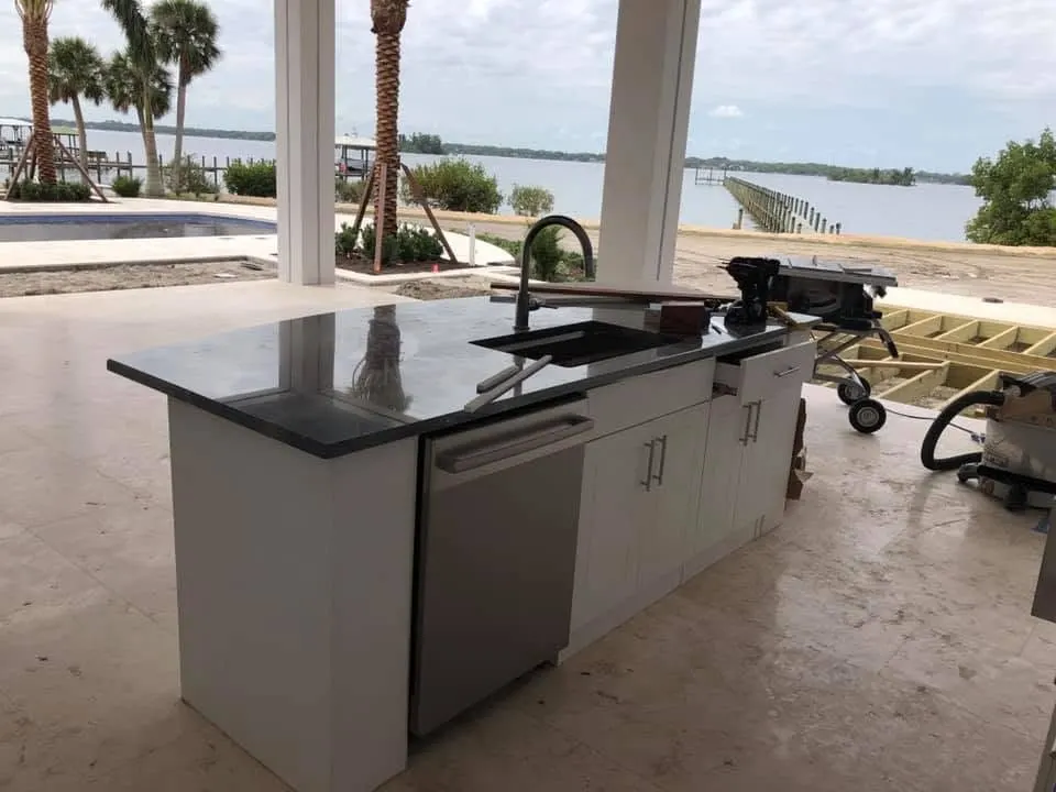Outdoor kitchen island with a sink and dark stone top on a covered patio
