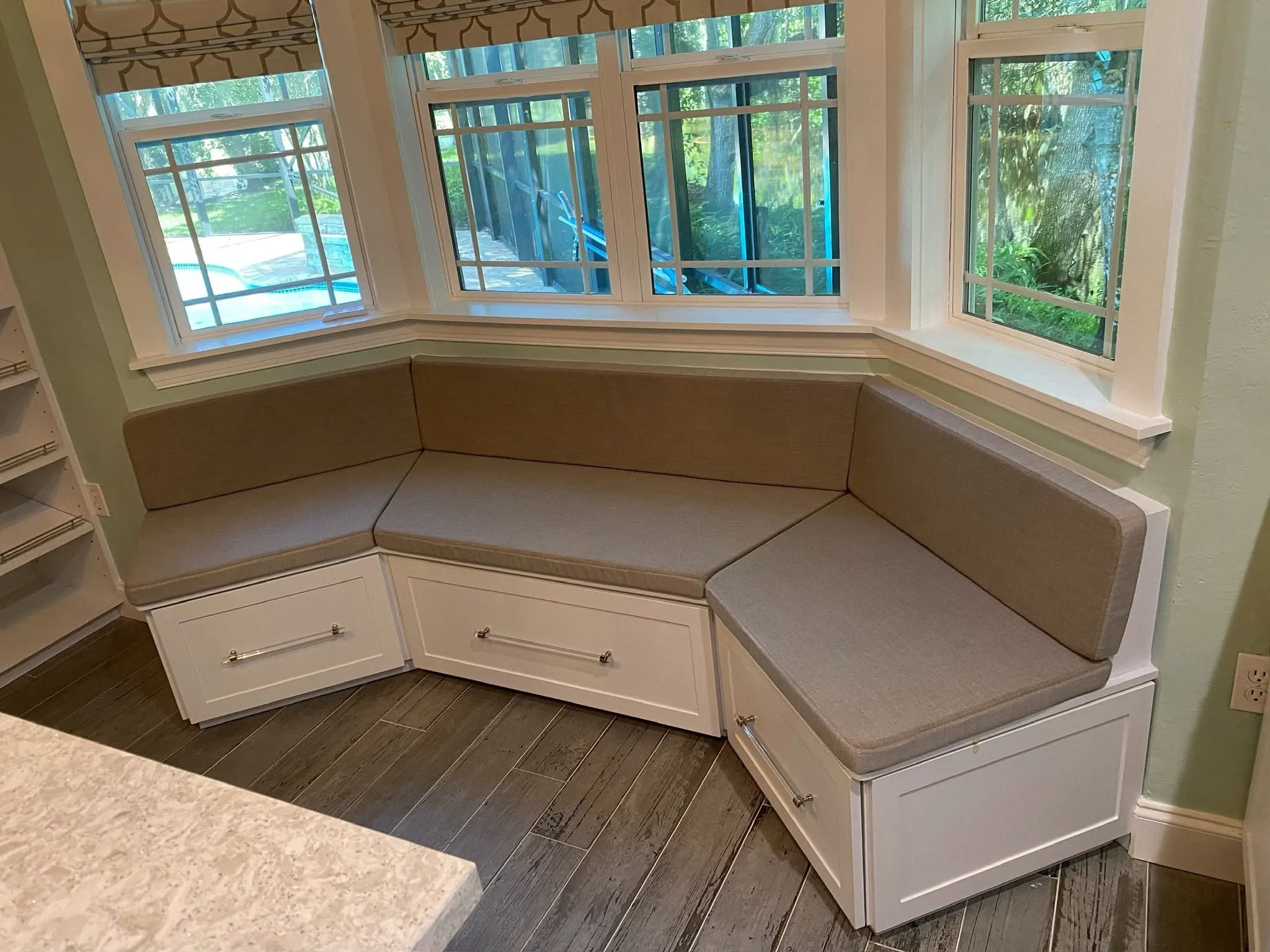 Upholstered window seat built into a bay window, with drawers underneath